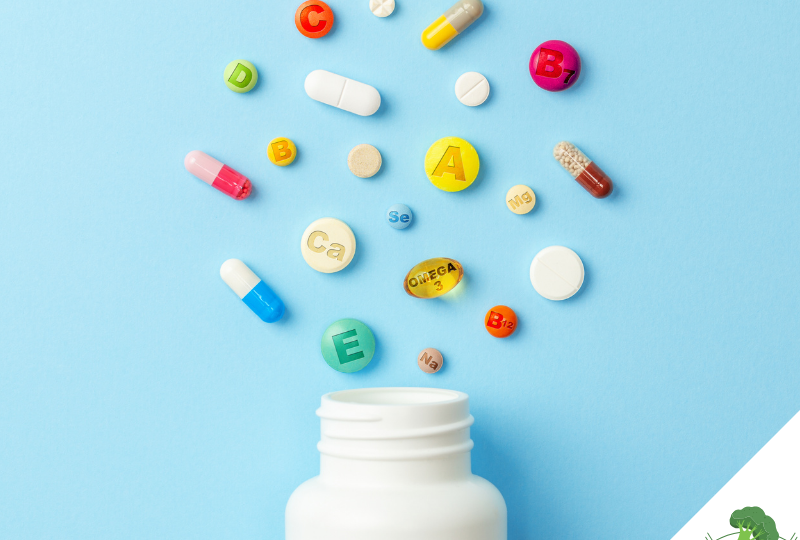 Eine offene weiße Pillendose vor einem blauen Hintergrund, aus der farbenfrohe Tabletten, Kapseln und Mikronährstoffe "herausfliegen". Auf den Pillen sind Symbole für Vitamine und Mineralstoffe wie A, B, C, D, E, Omega-3, Calcium (Ca), Magnesium (Mg) und Selen (Se) zu sehen. Die Szene repräsentiert die Bedeutung von Nahrungsergänzungsmitteln und Mikronährstoffen. In der unteren rechten Ecke befindet sich das Logo von **"Vegane Sporternährung für alle" by Anne Mayer**, dargestellt durch ein grünes Brokkoli-Icon.
