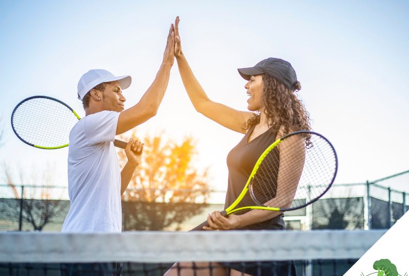 Ein Mann und eine Frau geben sich auf einem Tennisplatz ein High-Five, während sie Tennisschläger in der Hand halten. Beide tragen sportliche Kleidung und Kappen, und die Szene wird von warmem Sonnenlicht im Hintergrund erhellt. Das High-Five symbolisiert die Energie, Vitalität und den Teamgeist, die durch eine bewusste Lebensweise und Ernährung – wie der veganen Ernährung – gefördert werden können. Es unterstreicht die Aussage des Titels **"Sportliche Vorteile durch vegane Ernährung – Wissenschaftliche Einblicke und Erfahrungsberichte"**, indem es aufzeigt, wie eine ausgewogene pflanzliche Ernährung positive Auswirkungen auf Leistungsfähigkeit und Wohlbefinden im Sport haben kann. In der unteren rechten Ecke befindet sich das Logo von **"Vegane Sporternährung für alle" by Anne Mayer**, dargestellt durch ein grünes Brokkoli-Icon.
