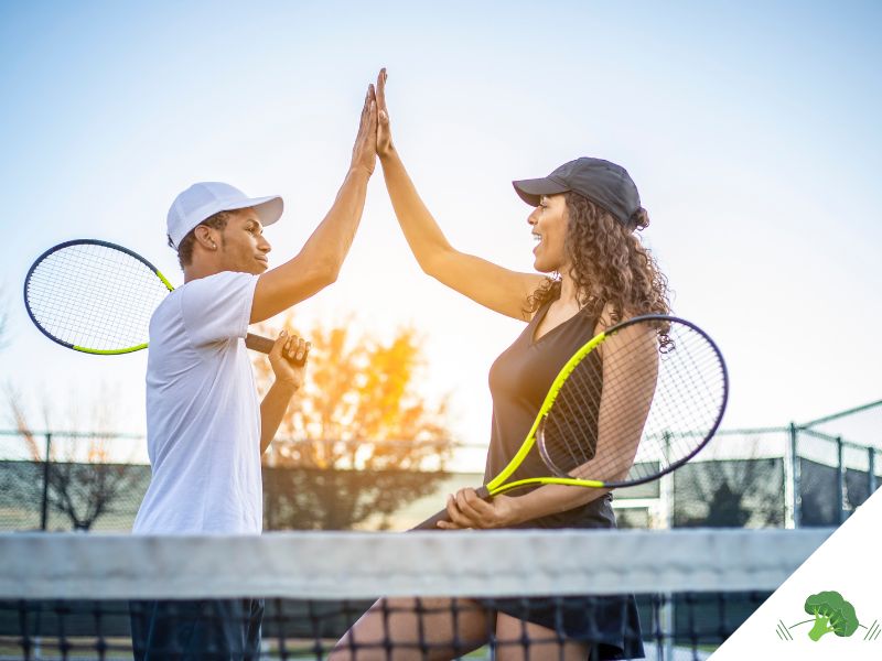 Ein Mann und eine Frau geben sich auf einem Tennisplatz ein High-Five, während sie Tennisschläger in der Hand halten. Beide tragen sportliche Kleidung und Kappen, und die Szene wird von warmem Sonnenlicht im Hintergrund erhellt. Das High-Five symbolisiert die Energie, Vitalität und den Teamgeist, die durch eine bewusste Lebensweise und Ernährung – wie der veganen Ernährung – gefördert werden können. Es unterstreicht die Aussage des Titels **"Sportliche Vorteile durch vegane Ernährung – Wissenschaftliche Einblicke und Erfahrungsberichte"**, indem es aufzeigt, wie eine ausgewogene pflanzliche Ernährung positive Auswirkungen auf Leistungsfähigkeit und Wohlbefinden im Sport haben kann. In der unteren rechten Ecke befindet sich das Logo von **"Vegane Sporternährung für alle" by Anne Mayer**, dargestellt durch ein grünes Brokkoli-Icon.