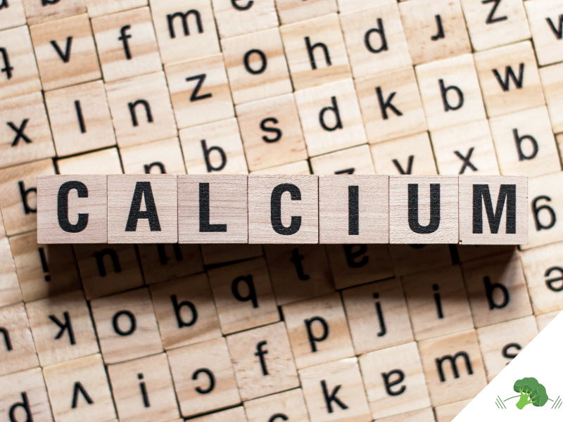 Holzklötze mit schwarzen Buchstaben darauf formen das Wort „CALCIUM“. Die Klötze liegen auf einer Fläche mit weiteren Holzklötzen, die verschiedene Buchstaben tragen.