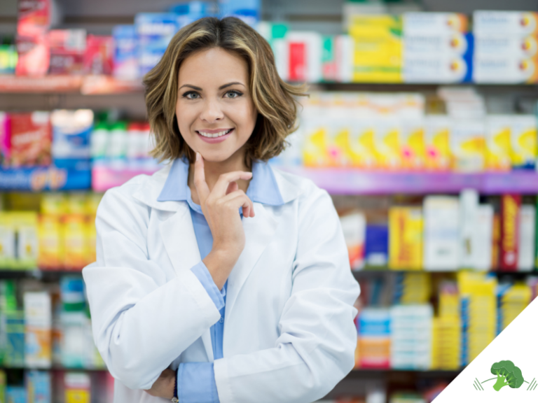 Eine junge Apothekerin steht lächelnd vor einem Regal mit Nahrungsergänzungsmitteln und Gesundheitsprodukten in einer Drogerie oder Apotheke. Sie trägt einen weißen Kittel und wirkt freundlich und kompetent.
