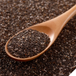 Holzlöffel mit einer Portion schwarzer und weißer Chiasamen, der auf einer großen Fläche verstreuter Chiasamen liegt.