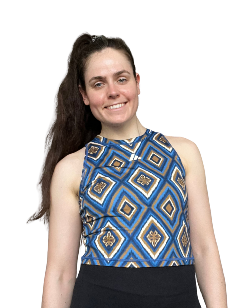 Anne Mayer lächelt in sportlicher Kleidung mit auffälligem, geometrisch gemustertem Top in Blau-, Braun- und Weißtönen – als sympathische Expertin für vegane Sporternährung.
