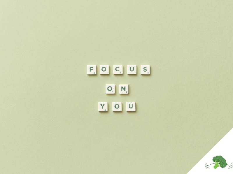 Scrabble-Buchstaben auf einem hellgrünen Hintergrund formen die Worte „FOCUS ON YOU“ in drei Zeilen, unten rechts befindet sich ein freier Bereich mit weißem Dreieck und einer Illustration eines grünen Brokkoli mit Hanteln.