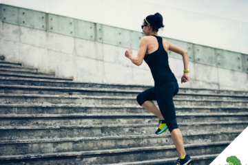 Frau in Sportkleidung läuft dynamisch eine breite Steintreppe hoch; sie trägt Sonnenbrille und Sportuhr, der Hintergrund zeigt eine moderne Betonfassade – Symbol für Aktivität, Fortschritt und körperliche Leistungsbereitschaft.