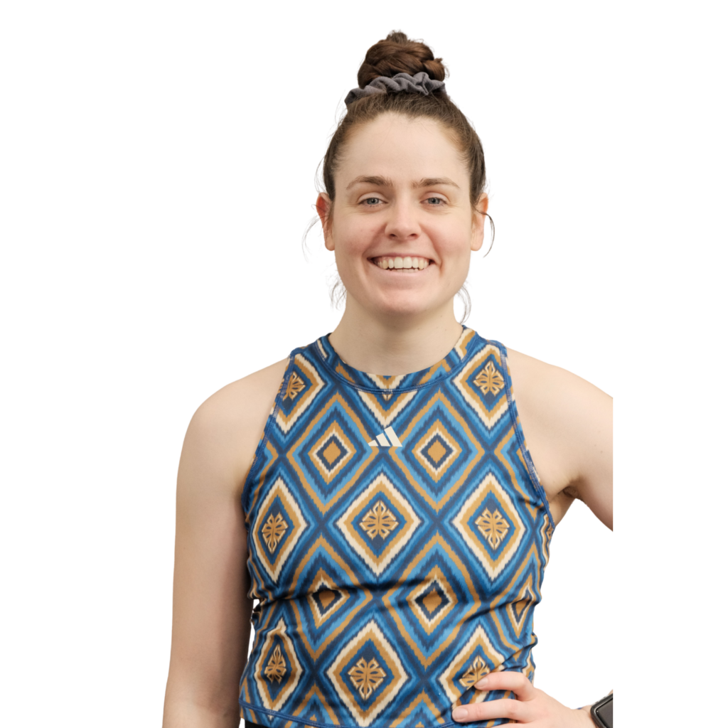 Porträt einer lächelnden Frau mit hochgesteckten Haaren vor schwarzem Hintergrund, sie trägt ein ärmelloses blau-gelb gemustertes Sporttop und steht selbstbewusst mit einer Hand in der Hüfte.