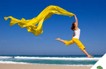 Frau springt kraftvoll und frei am Strand in die Luft, ein leuchtend gelbes Tuch weht dynamisch über ihr – Symbol für Leichtigkeit, Energie und die befreiende Wirkung eines beschwerdefreien Körpers.
