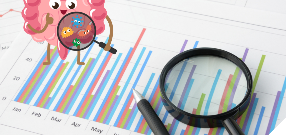 Fröhlich gezeichneter Darm mit Lupe betrachtet bunte Bakterien vor einem Hintergrund aus bunten Balken- und Kreisdiagrammen sowie Zahlen, daneben liegen eine echte Lupe und ein Stift auf einem Datenblatt.