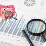 Fröhlich gezeichneter Darm mit Lupe betrachtet bunte Bakterien vor einem Hintergrund aus bunten Balken- und Kreisdiagrammen sowie Zahlen, daneben liegen eine echte Lupe und ein Stift auf einem Datenblatt.