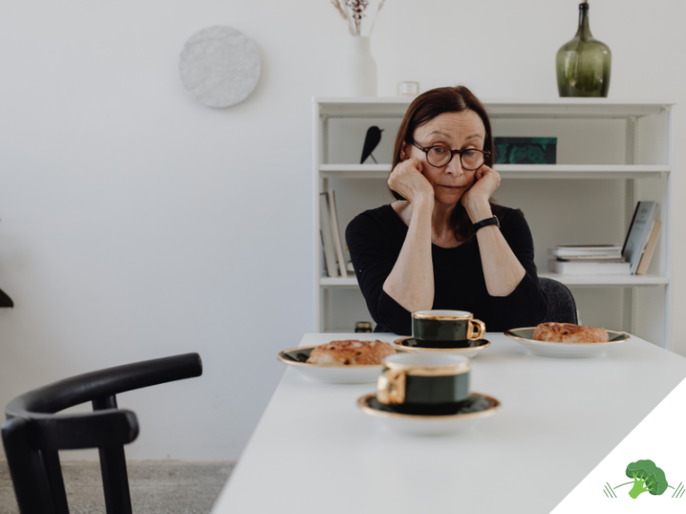 Überforderte Frau sitzt nachdenklich an einem Tisch mit Kaffee und Gebäck und wirkt unsicher oder blockiert bei einer Entscheidung rund um Ernährung oder Alltag