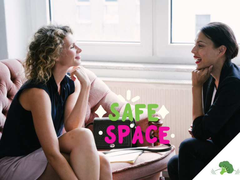 Zwei Frauen sitzen sich in einem hellen Raum auf einem Sofa gegenüber und unterhalten sich lächelnd. Im Vordergrund steht der farbige Schriftzug „Safe Space“.